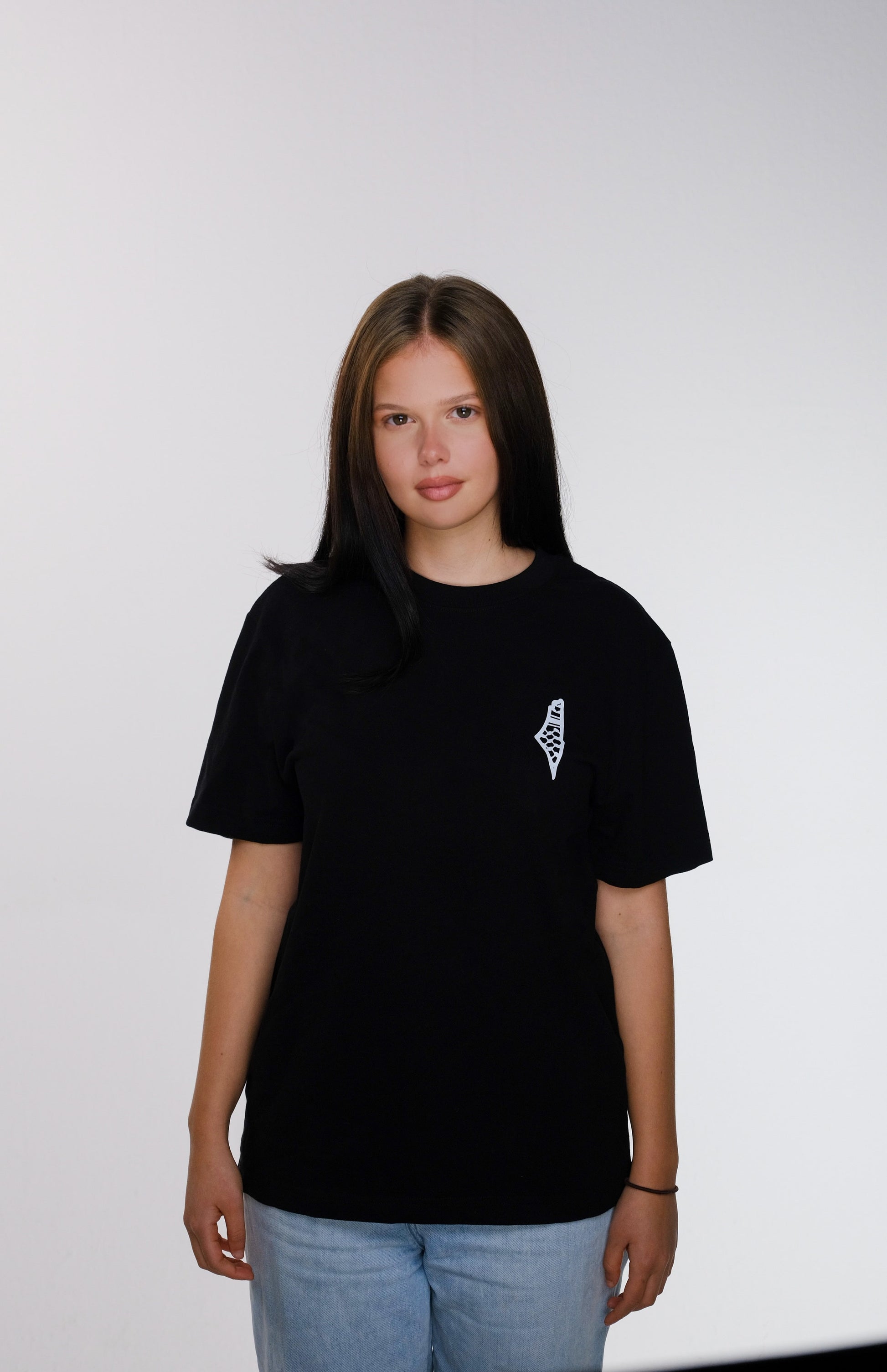 Front view of the model wearing the black Palestine Brand Logo T-shirt, featuring a minimalist design with a small map of Palestine on the right chest. The logo is inspired by the colors of the traditional keffiyeh. The back of the T-shirt is plain black.