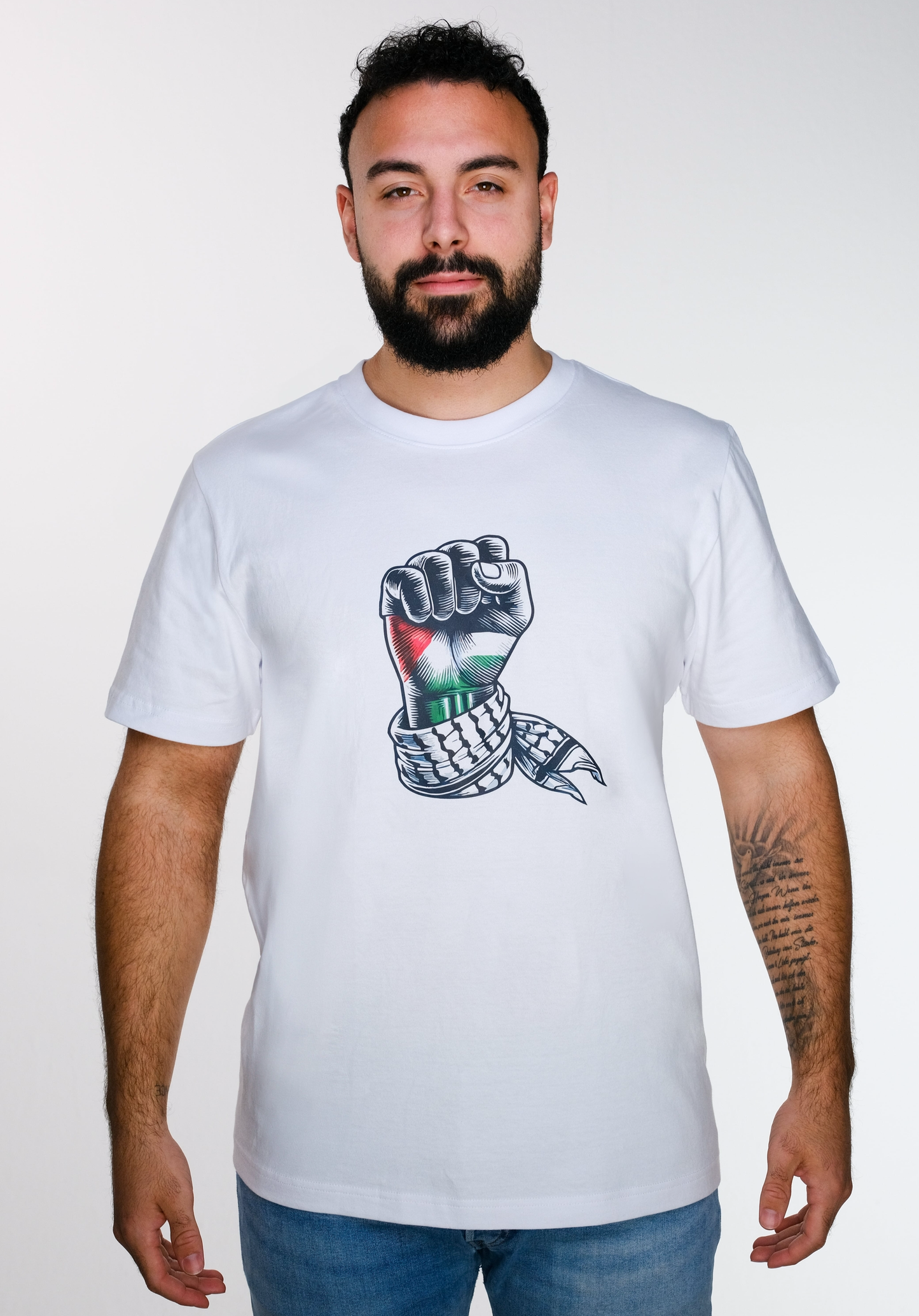 Model front view of a model wearing a white sumud T-shirt featuring a raised fist, colored with the Palestinian flag, wrapped in a Palestinian keffiyeh.