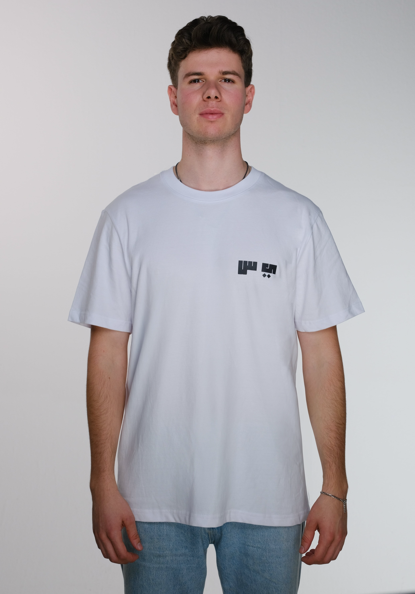 Front view of model wearing a white Resist T-shirt, featuring the Arabic letters "ي" and "س" subtly printed on the right chest, symbolizing resistance.