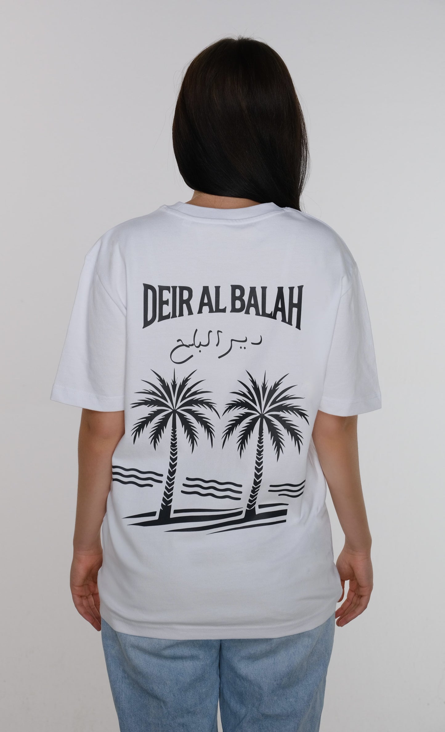 Model wearing the Deir al-Balah T-shirt, back view showcasing the length and drape of the fabric, with a date palm tree design symbolizing the city's heritage.