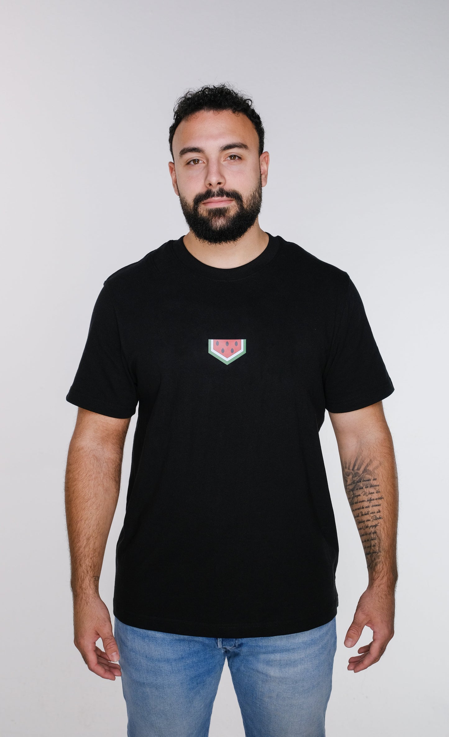 A model wearing the watermelon T-shirt, standing confidently.
 The red-green-black colors of the watermelon design evoke the Palestinian flag and resistance.